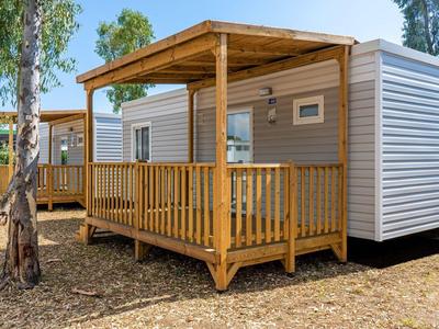 Stacaravan met houten veranda en dak op camping met bomen.