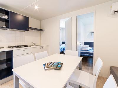 Moderne keuken en eetgedeelte met wit meubilair en twee slaapkamers op de achtergrond