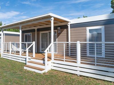 Modern klein huis met veranda en reling op groen gazon onder blauwe lucht.