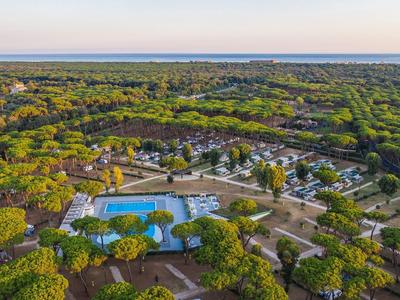 Luchtfoto van een rustige camping met een zwembad en veel groene bomen bij zonsondergang.