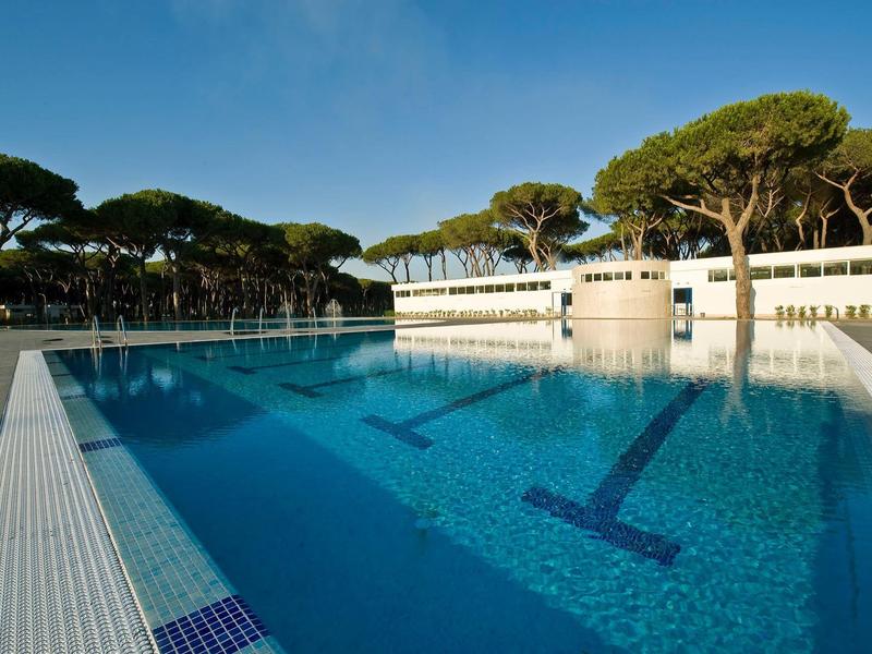 Buitenzwembad van een hotel met bomen op de achtergrond bij heldere lucht.