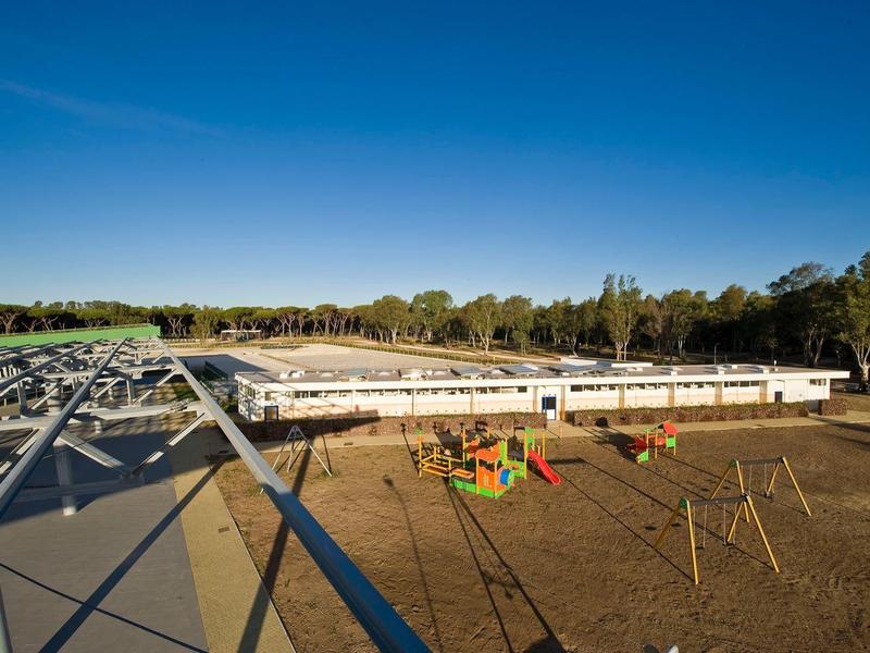Groot terrein met modern, langgerekt vakantiecomplex en speeltuin onder een blauwe lucht.