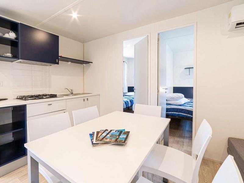 Moderne keuken en eetgedeelte met wit meubilair en twee slaapkamers op de achtergrond