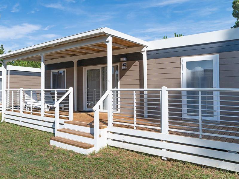 Modern klein huis met veranda en reling op groen gazon onder blauwe lucht.
