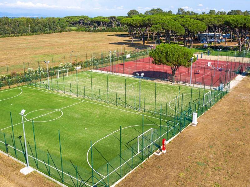 Meerdere sportvelden, waaronder een voetbalveld en tennisbanen, omgeven door bomen en velden.
