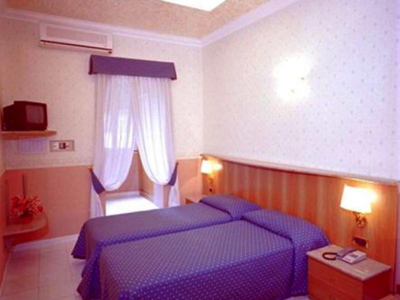 Hotel room with two single beds, purple bedspreads, and a window with white curtains.