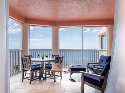 Balkon mit blauem Meerblick, Tisch und Stühlen sowie zwei blauen Lounge-Sesseln bei Tageslicht.
