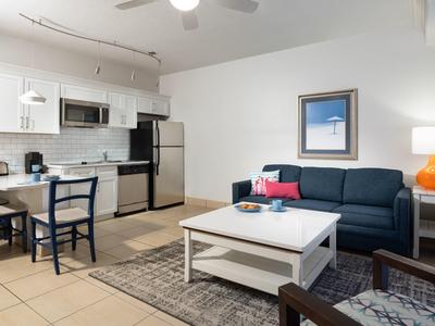 Helle Wohnküche mit moderner weißer Küche, blauer Couch, springender Lampe und Teppich auf Fliesen.