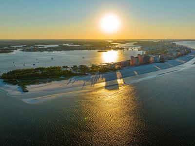 Luftaufnahme einer Insel mit Gebäuden und Stränden bei Sonnenuntergang über ruhigem Wasser.