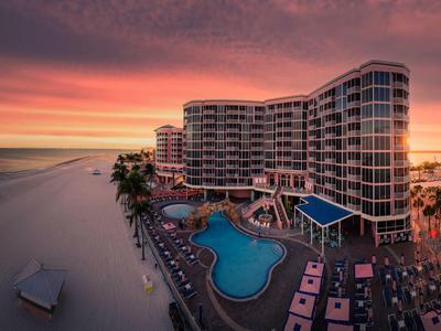 Großes Hotel am Strand mit Pool, Liegestühlen und farbigem Himmel bei Sonnenuntergang.