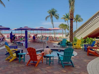 Bunte Stühle und Tische auf Terrasse mit Palmen, Sonnenschirmen und blauen Himmel am Strand.