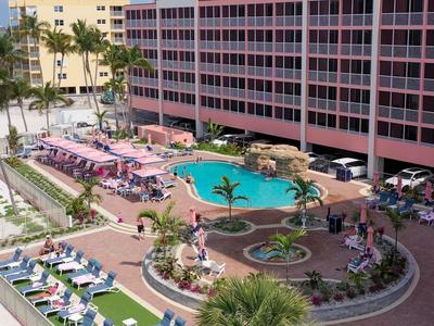 Ein großer Außenpool mit Liegestühlen und Palmen neben einem hohen Hotelgebäude.