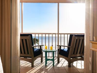 Zwei Stühle und ein kleiner Tisch mit Getränken auf Balkon mit Meerblick bei Sonnenschein.