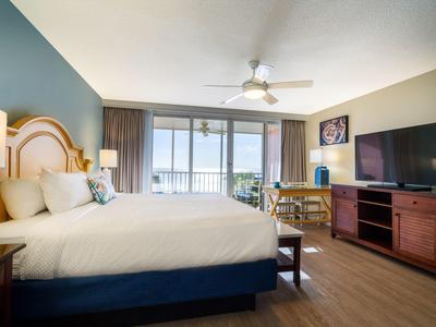 Geräumiges Hotelzimmer mit großem Bett, Holzmobiliar, Ventilator und Balkon mit Meerblick.