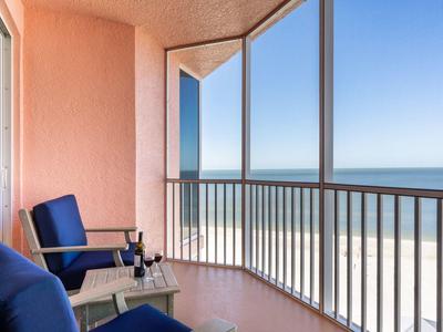 Balkon mit blauen Stühlen, Tisch und Meerblick unter klarem blauem Himmel.