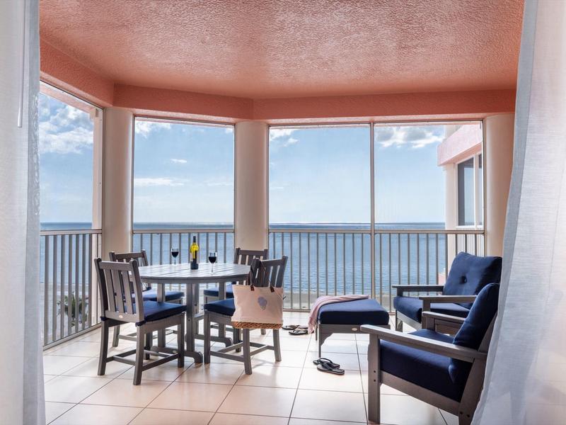 Balkon mit blauem Meerblick, Tisch und Stühlen sowie zwei blauen Lounge-Sesseln bei Tageslicht.