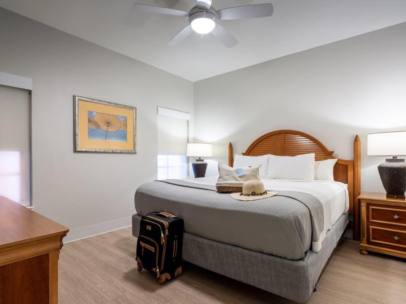 Modernes Schlafzimmer mit großem Bett, Nachttischlampe, Koffer und Deckenventilator an der Decke.