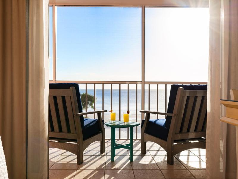 Zwei Stühle und ein kleiner Tisch mit Getränken auf Balkon mit Meerblick bei Sonnenschein.