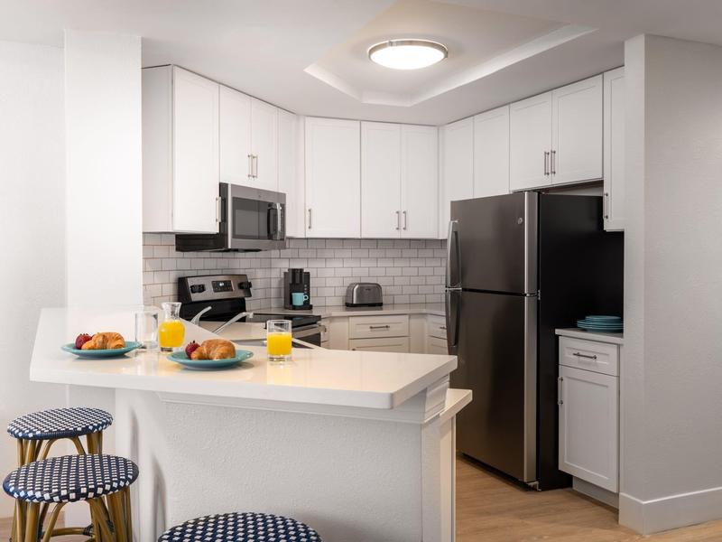 Moderne helle Küche mit weißem Schrankdesign, schwarzem Kühlschrank und Frühstückstheke mit gestreiften Hockern.