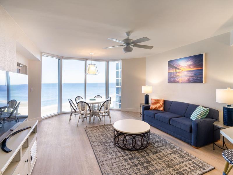 Helles Wohnzimmer mit blauer Couch, runden Tischen, Teppich und großem Fenster mit Meerblick.