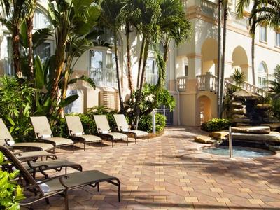 Sitzbereich mit Liegestühlen und Palmen neben einem Hotel mit Springbrunnen.