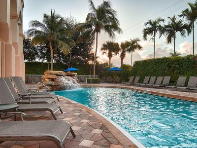 Area piscina dell'hotel con sedie a sdraio e palme al tramonto.