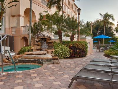 Gemütlicher Garten mit Pool, Wasserfall, Liegen und blauem Sonnenschirm neben Wohnhaus.