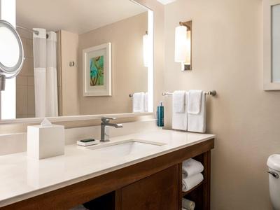 Helles Badezimmer mit weißer Arbeitsplatte, großem Spiegel, Handtüchern und moderner Beleuchtung.