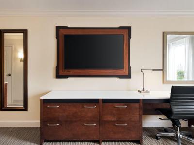 Moderner Büroraum mit braunem Schreibtisch, schwarzem Stuhl, Spiegel und Wandbild.