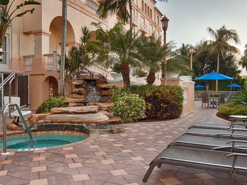 Gemütlicher Garten mit Pool, Wasserfall, Liegen und blauem Sonnenschirm neben Wohnhaus.