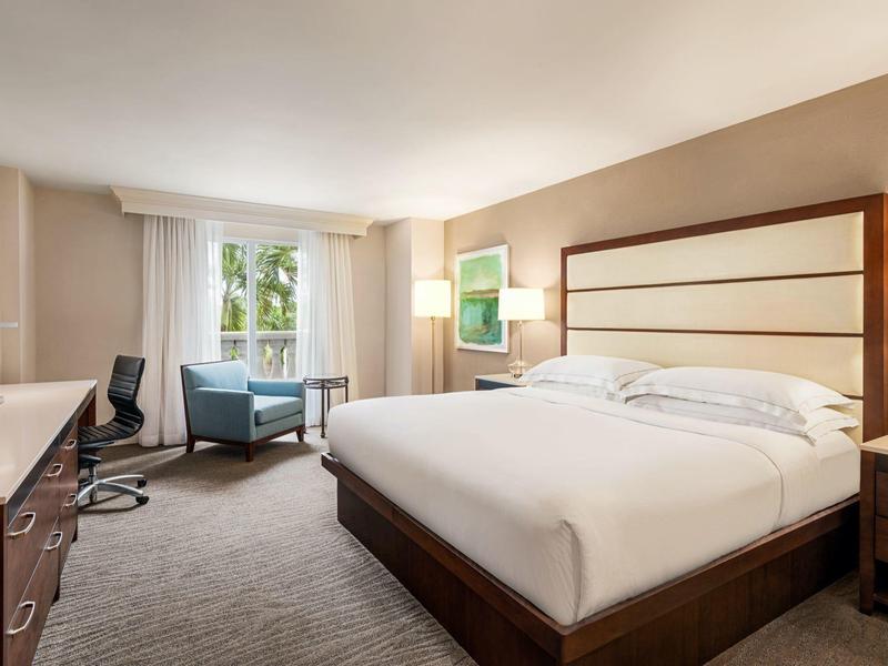 Helles, modernes Schlafzimmer mit großem Bett, grauem Teppich, Fenster und Sitzbereich mit zwei Sesseln.