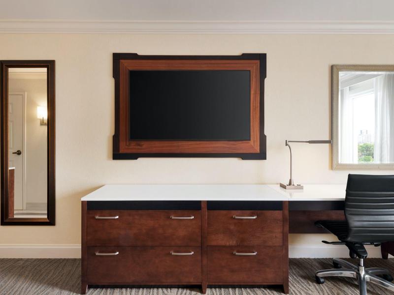 Moderner Büroraum mit braunem Schreibtisch, schwarzem Stuhl, Spiegel und Wandbild.