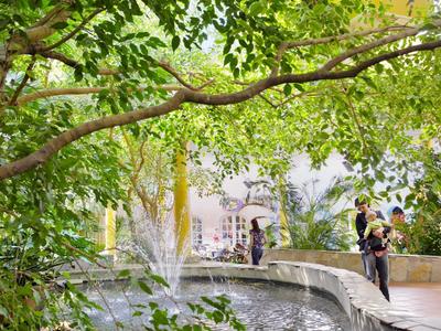 Menschen stehen an einer Brücke über einem Teich mit Springbrunnen in einem grünen Park.