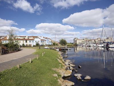 Marina mit Booten, Häusern und Gehweg unter blauem Himmel mit Wolken.