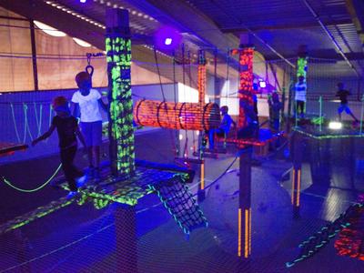 Innenbereich mit beleuchtetem Kletterpark und Hindernissen in dunklem Ambiente