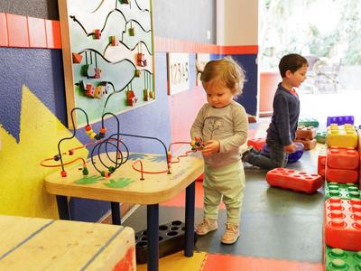 Kinder spielen mit Lernspielzeug und großen Bausteinen in einem bunten Spielzimmer.