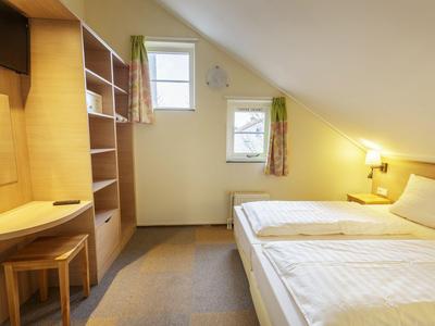 Helles Hotelzimmer mit zwei Einzelbetten, Holzmöbeln und Dachschräge.