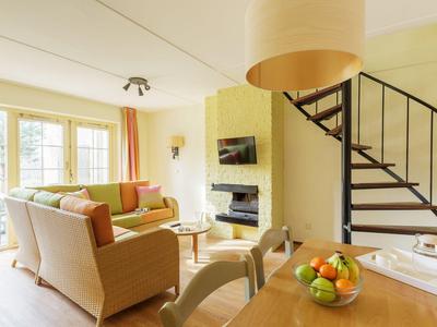 Helles Wohnzimmer mit Sofa, Kamin, TV und Wendeltreppe zu einer oberen Etage.