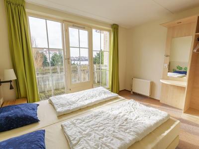 Ein helles Schlafzimmer mit zwei Einzelbetten, grünen Vorhängen und großem Fenster mit Blick nach draußen.