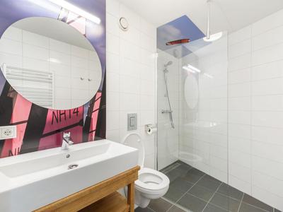 Helles Badezimmer mit rundem Spiegel, Waschbecken, WC und begehbarer Dusche mit Glasabtrennung.