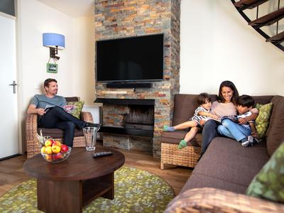 Gemütliches Wohnzimmer mit zwei Personen auf Körbchensofas neben Kamin und Flachbildfernseher.