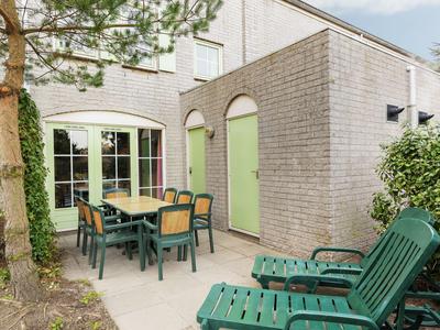 Terrasse mit grünem Möbelset und Liegestühlen vor einem weißen Gebäude mit grünen Türen und Fenstern.
