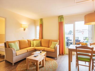 Helles Wohnzimmer mit Ecksofa, Couchtischen und Essbereich neben großem Fenster.