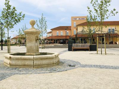 Ein offener Platz mit einem Brunnen im Vordergrund und einem Hotelgebäude im Hintergrund bei klarem Himmel.
