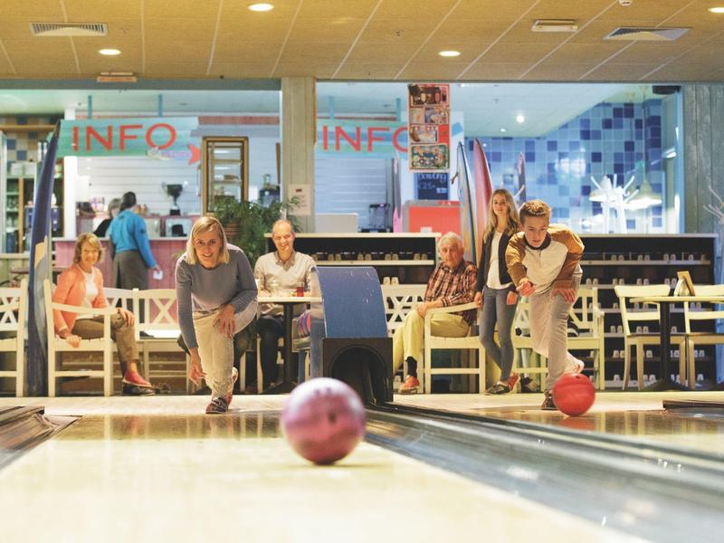 Bunte Bowlingkugeln rollen auf Bahnen, Menschen sitzen und beobachten entspannt im Hintergrund.