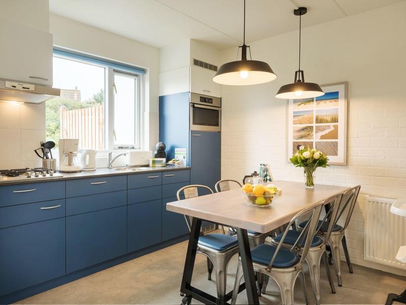 Moderne Küche mit blauen Unterschränken, Holztisch, Metallstühlen und großen Fenstern.