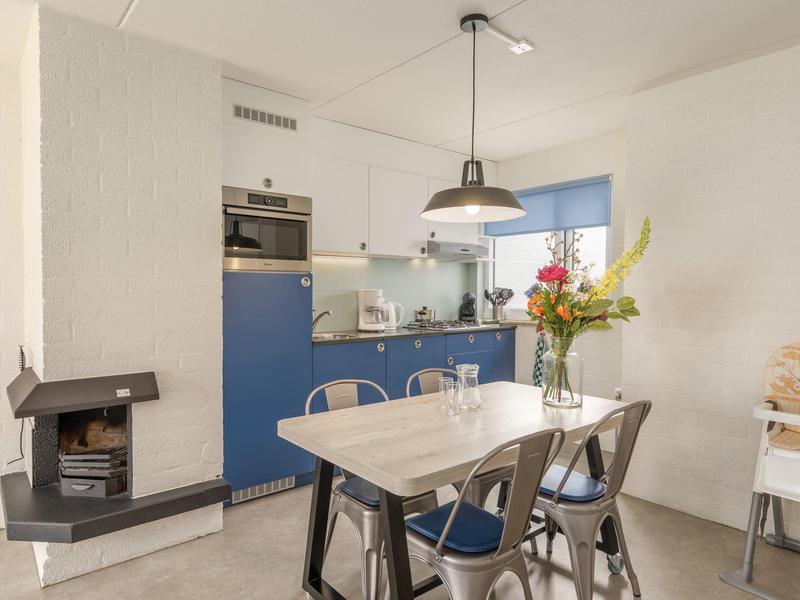 Moderner Essbereich mit weißem Tisch, Metallstühlen, Kamin und Küchenzeile mit blauen Schränken.