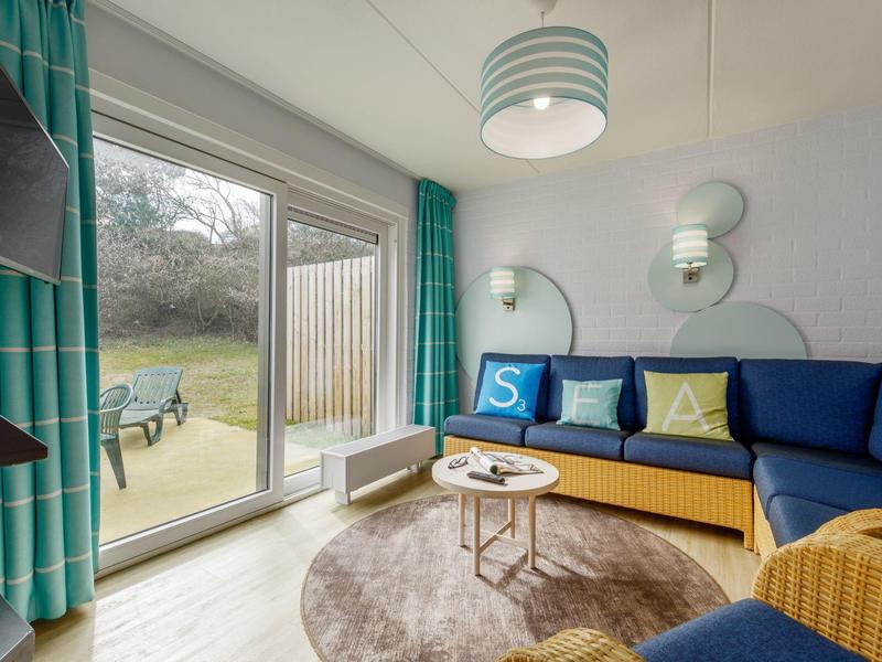 Helles Wohnzimmer mit blauer Eckcouch, runden Teppich, großen Fenstern und türkisfarbenen Vorhängen.