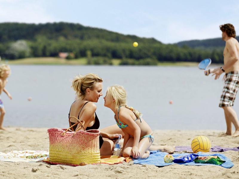 Familia con niños juega y se relaja en la orilla arenosa del lago en un día soleado.