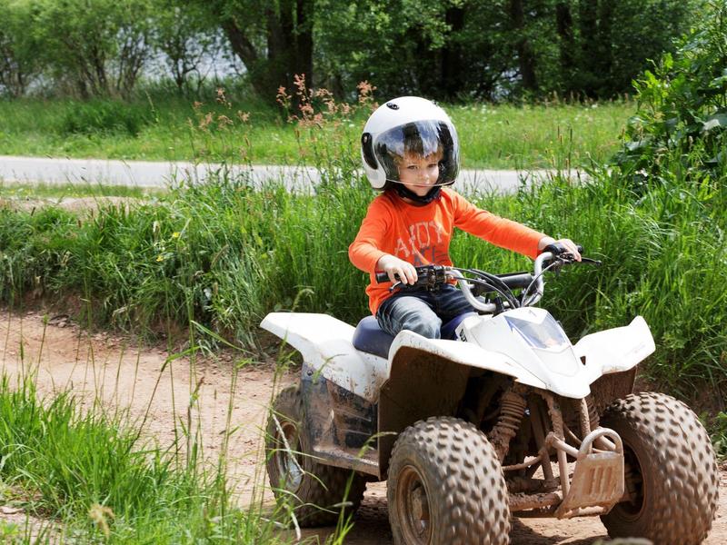 Niño con casco conduciendo un quad en un camino rural en paisaje verde.